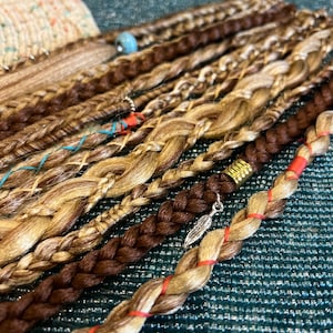 Puede incluir: Una colección de extensiones de cabello trenzado en tonos marrones y rubios. Las extensiones están decoradas con cuentas y plumas.