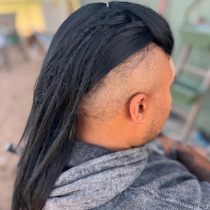 Peut inclure: Une personne portant un sweat à capuche gris avec de longues dreadlocks noires. Les dreadlocks sont coiffées avec une raie sur le côté et des côtés rasés. La personne est de dos.