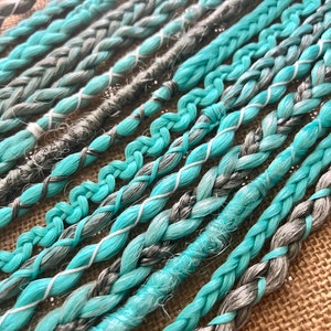 May include: A collection of teal and gray braided hair extensions. The extensions are arranged in rows, with the teal strands on top of the gray strands.
