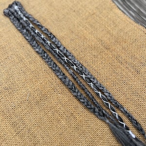 Op de afbeelding: Vier zwarte en witte gevlochten haarextensies met witte stiksels.