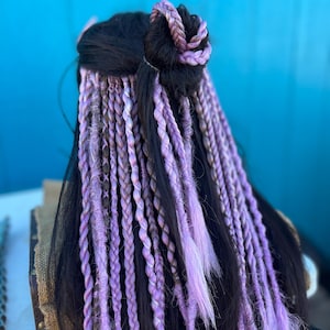 May include: A long, black wig with purple and white braids. The braids are tied up in a bun at the top of the head.