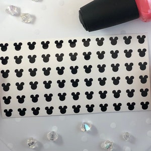 May include: A sheet of black Mickey Mouse head stickers. The stickers are arranged in a grid pattern on a white background.