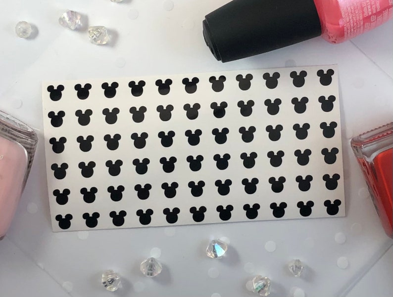 May include: A sheet of black Mickey Mouse head stickers. The stickers are arranged in a grid pattern on a white background.