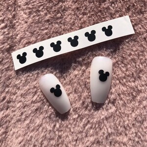 May include: A sheet of black Mickey Mouse head nail stickers with two white fake nails with black Mickey Mouse head stickers on them.