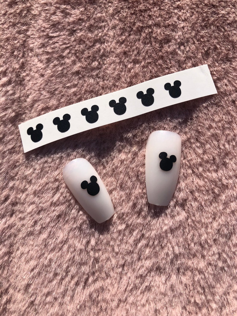 May include: A sheet of black Mickey Mouse head nail stickers with two white fake nails with black Mickey Mouse head stickers on them.
