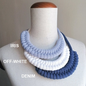 Puede incluir: Un collar de crochet de tres hebras en tonos azules y blancos. El collar est&aacute; hecho de cuerda de algod&oacute;n y presenta un dise&ntilde;o en capas con los colores "Iris", "Blanco roto" y "Denim" etiquetados debajo.
