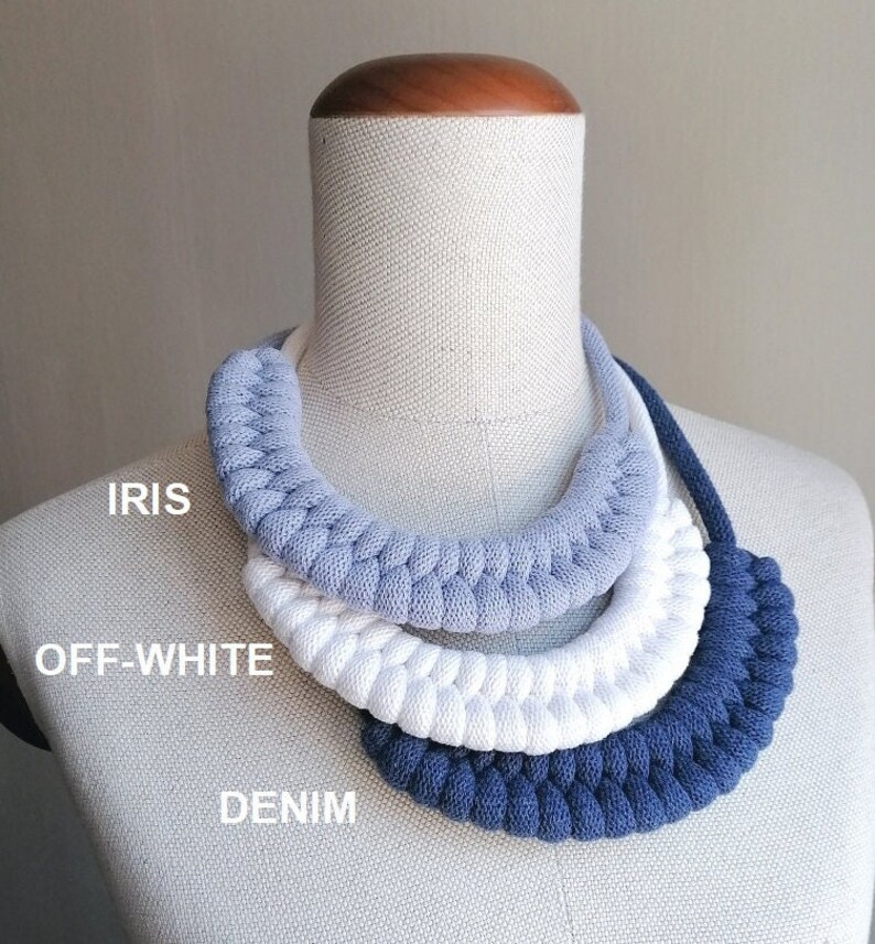 Puede incluir: Un collar de crochet de tres hebras en tonos azules y blancos. El collar est&aacute; hecho de cuerda de algod&oacute;n y presenta un dise&ntilde;o en capas con los colores "Iris", "Blanco roto" y "Denim" etiquetados debajo.