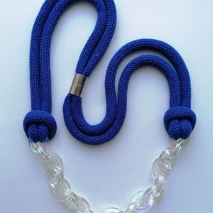 Op de afbeelding: Een blauwe touwketting met een transparante plastic ketting. Het touw is aan beide uiteinden geknoopt en de ketting is met een metalen sluiting aan het touw bevestigd.