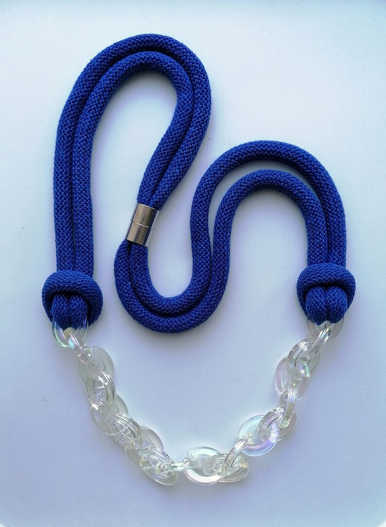 Op de afbeelding: Een blauwe touwketting met een transparante plastic ketting. Het touw is aan beide uiteinden geknoopt en de ketting is met een metalen sluiting aan het touw bevestigd.