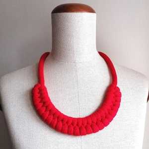 Puede incluir: Un collar de cuerda roja con un dise&ntilde;o trenzado. El collar se muestra en un maniqu&iacute; blanco.