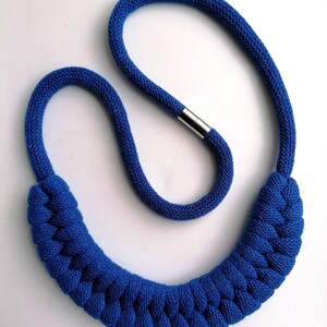 Puede incluir: Un collar de cuerda trenzada azul con un cierre plateado. El collar est&aacute; hecho de una cuerda gruesa y suave y tiene un dise&ntilde;o simple y elegante.