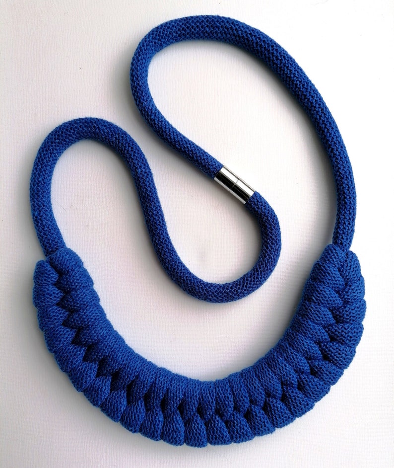 Puede incluir: Un collar de cuerda trenzada azul con un cierre plateado. El collar est&aacute; hecho de una cuerda gruesa y suave y tiene un dise&ntilde;o simple y elegante.