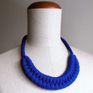 Puede incluir: Un collar de cuerda trenzada azul real en un maniqu&iacute; blanco. El collar est&aacute; hecho de cuerda gruesa y tiene un dise&ntilde;o simple y elegante.