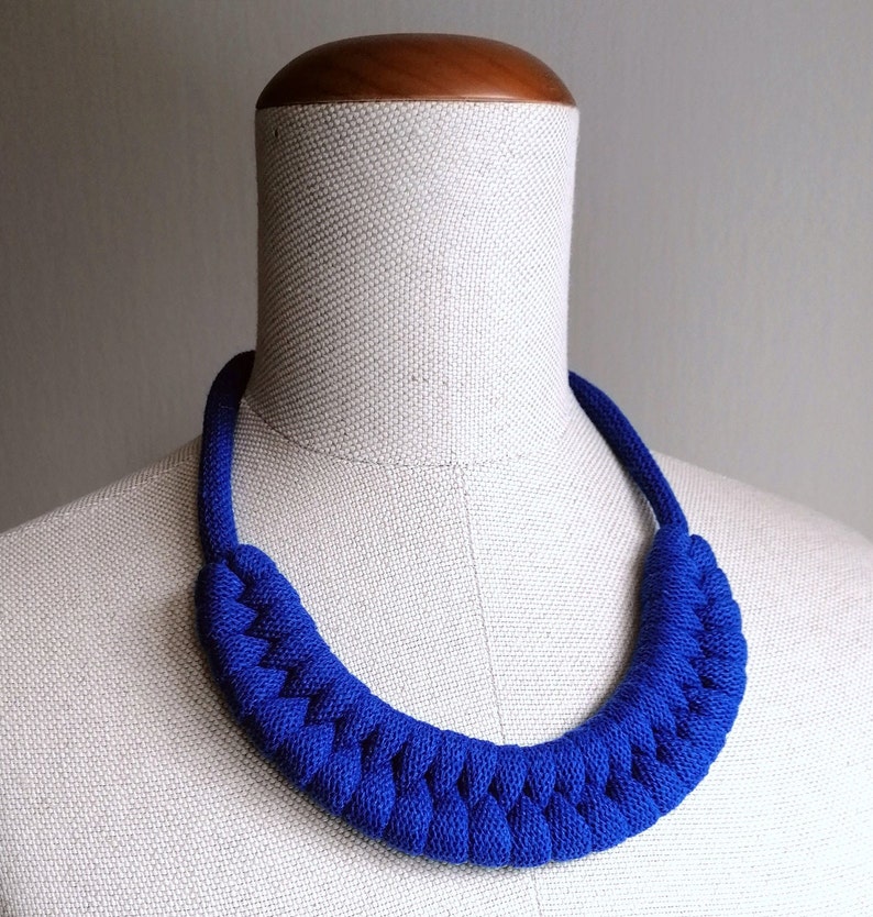 Puede incluir: Un collar de cuerda trenzada azul real en un maniqu&iacute; blanco. El collar est&aacute; hecho de cuerda gruesa y tiene un dise&ntilde;o simple y elegante.