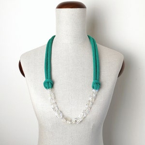 Op de afbeelding: Een groene touwketting met een transparante plastic ketting. De ketting wordt getoond op een wit mannequin.