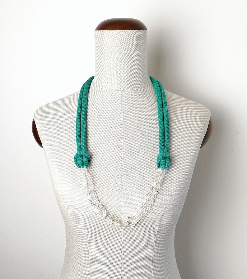Op de afbeelding: Een groene touwketting met een transparante plastic ketting. De ketting wordt getoond op een wit mannequin.