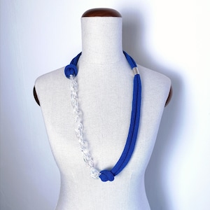 Op de afbeelding: Een blauwe en transparante plastic ketting met een zilveren accent. De ketting wordt getoond op een wit mannequin.