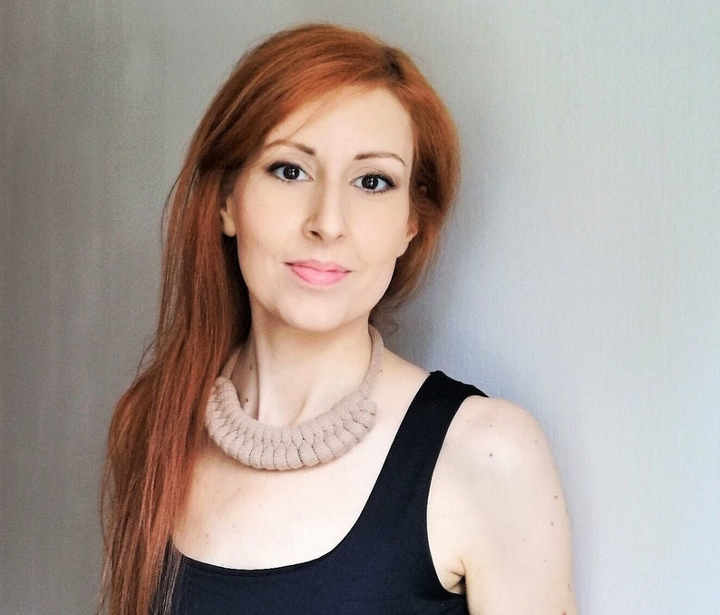 Puede incluir: Una mujer con el pelo largo y rojo que lleva un top negro de tirantes y un collar de ganchillo beige.