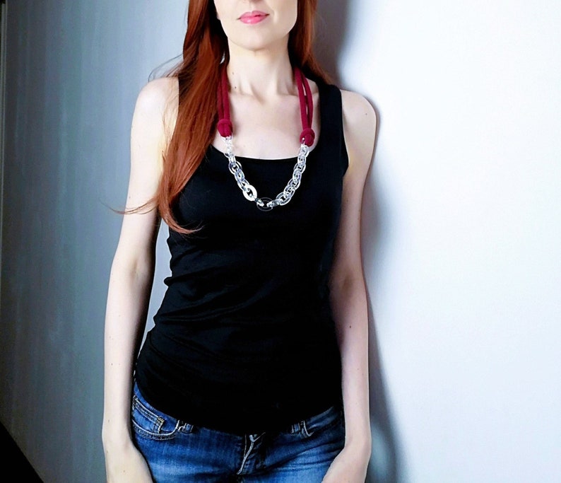Op de afbeelding: Een vrouw draagt een zwart tanktop en een blauwe jeans met een lange, rode en doorzichtige kettingketting.