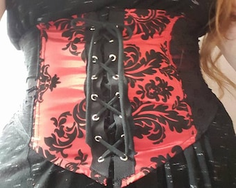 May include: A black corset with a red satin panel featuring a black floral pattern. The corset has a black lace-up front with silver eyelets.