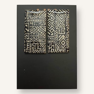 May include: Two rectangular wall art pieces with a black background. Each piece features a geometric pattern in silver and black. The art is mounted on a larger black rectangular board.
