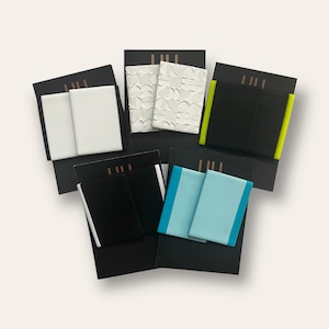 Puede incluir: Seis pares de pendientes expuestos en tarjetas negras. Los pendientes están hechos de diferentes materiales y colores, incluyendo blanco, negro, azul y verde.