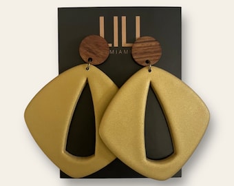 May include: Gold statement earrings with a geometric shape and a cutout design. The earrings are attached to a wooden circle.