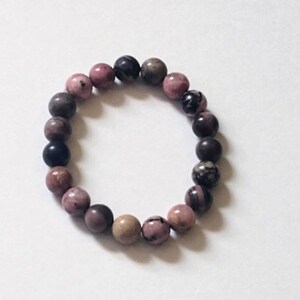 May include: A pink, black, and brown beaded bracelet. The beads are round and have a natural, polished look.