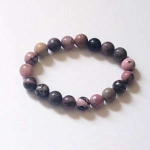 May include: A pink, brown, and black beaded bracelet with round, smooth stones.