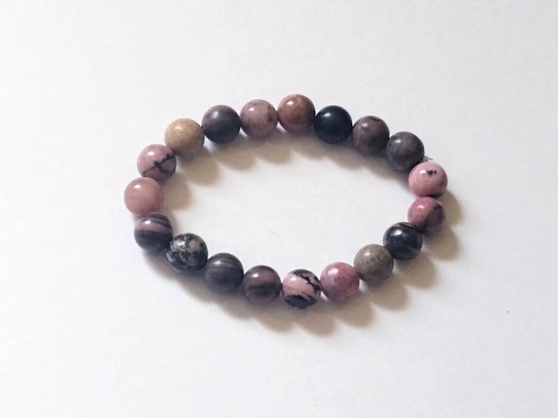May include: A pink, brown, and black beaded bracelet with round, smooth stones.