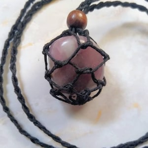 May include: A pink and white gemstone pendant with a black macrame knotting, hanging from a black cord necklace.
