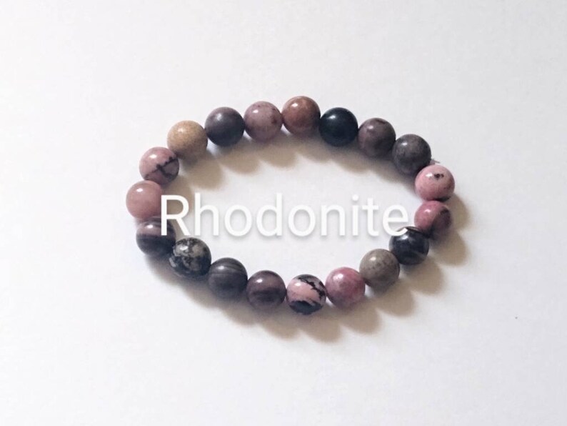 May include: A pink, brown, and black rhodonite gemstone bracelet. The bracelet is made of round beads and is strung on elastic.