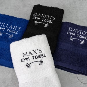 Pu&ograve; includere: Quattro asciugamani da palestra personalizzati in diversi colori: blu, nero, bianco e blu navy. Ogni asciugamano ha un design ricamato bianco con il nome del proprietario e le parole "Gym Towel" con un simbolo di bilanciere.