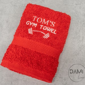 Pu&ograve; includere: Asciugamano da palestra rosso con ricamo bianco che dice "Tom's Gym Towel" con un grafico di manubri.
