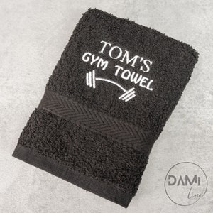 Pu&ograve; includere: Asciugamano da palestra nero con ricamo bianco che dice "Tom's Gym Towel" e un grafico di bilanciere.