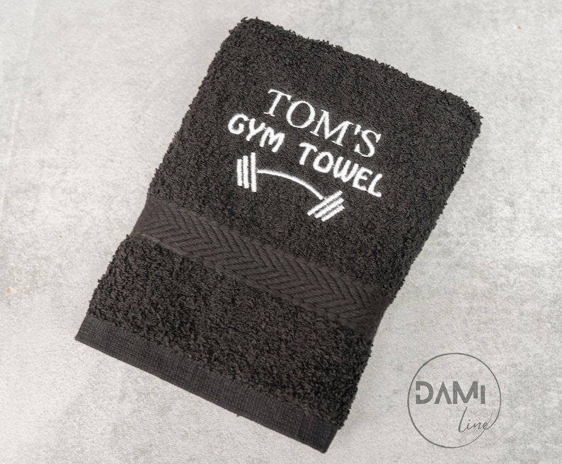 Pu&ograve; includere: Asciugamano da palestra nero con ricamo bianco che dice "Tom's Gym Towel" e un grafico di bilanciere.