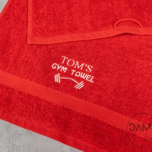 Pu&ograve; includere: Asciugamano da palestra rosso con ricamo bianco che dice "Tom's Gym Towel" con una grafica di bilanciere.