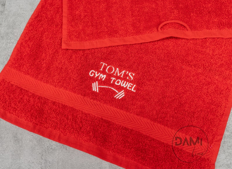Pu&ograve; includere: Asciugamano da palestra rosso con ricamo bianco che dice "Tom's Gym Towel" con una grafica di bilanciere.