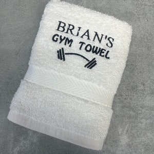 Pu&ograve; includere: Asciugamano da palestra in cotone bianco con ricamo nero che recita "BRIAN'S GYM TOWEL" e un grafico di un manubrio.