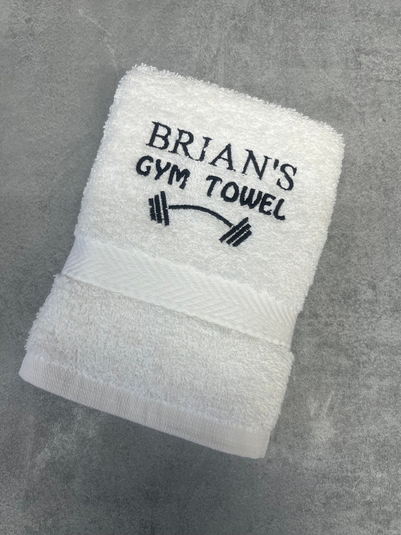 Pu&ograve; includere: Asciugamano da palestra in cotone bianco con ricamo nero che recita "BRIAN'S GYM TOWEL" e un grafico di un manubrio.