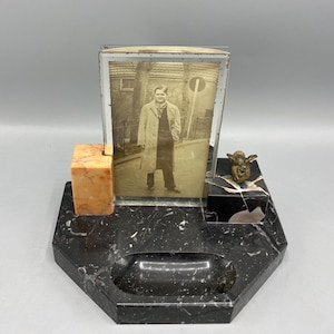 Op de afbeelding: Art Deco zwart marmeren fotolijst met een sepia foto. De lijst heeft een klein oranje marmeren blok en een klein bronzen beeld. De basis heeft een kleine asbak.