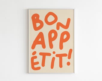 May include: A framed art print with the words "BON APPÉTIT!" in orange, handwritten-style lettering. The text is centered on a cream-colored background. The frame is silver.