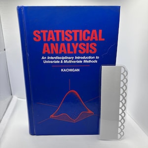 May include: A blue book titled "STATISTICAL ANALYSIS" with red lettering and a red graph illustration. The book is accompanied by a white, decorative, rectangular object with a scalloped edge.