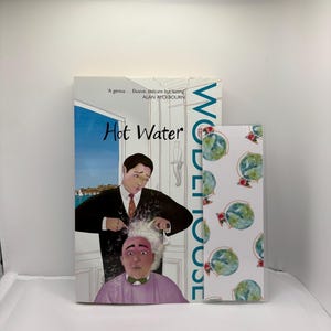 May include: A book titled "Hot Water" with a cover illustration of a man cutting another man's hair. A smaller book with a globe pattern is next to it. The author's name is Alan Ayckbourn.