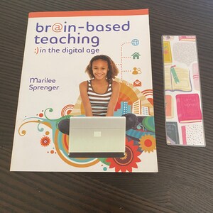 May include: A book titled "br@in-based teaching :) in the digital age" by Marilee Sprenger. The cover features a young girl using a laptop computer with a colorful background.