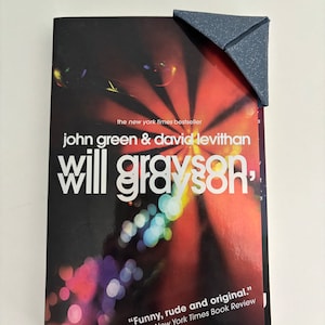May include: A paperback book with a colorful, abstract cover featuring a blurred image of a stage with lights. The title of the book is "Will Grayson," and the authors are John Green and David Levithan. The book is a New York Times bestseller and has a quote from The New York Times Book Review that reads "Funny, rude and original."