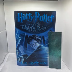May include: A hardcover book titled "Harry Potter and the Order of the Phoenix" with a blue cover featuring an illustration of Harry Potter. A matching bookmark with a galaxy design is next to the book.