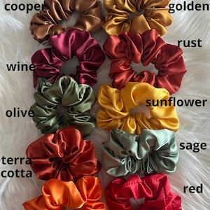 May include: A collection of satin scrunchies in various colors, including copper, golden, wine, rust, olive, sunflower, terra cotta, sage, orange, and red. Each scrunchie is displayed with its color name in white text.