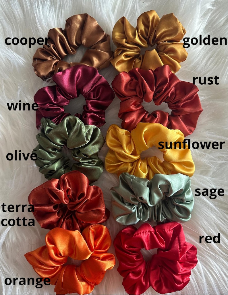 May include: A collection of satin scrunchies in various colors, including copper, golden, wine, rust, olive, sunflower, terra cotta, sage, orange, and red. Each scrunchie is displayed with its color name in white text.