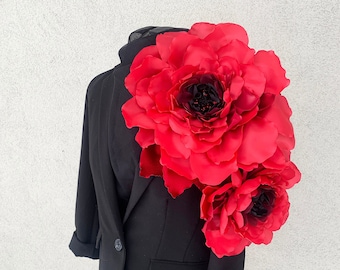 May include: A black blazer with a large red flower corsage. The flower has a dark red center and is made of fabric.